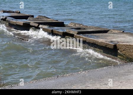 Wellen brechen gegen Betonpier an der felsigen Küste Stockfoto