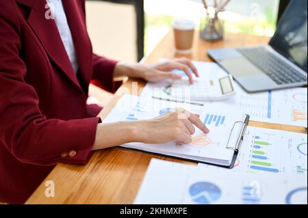 Professionelle Geschäftsfrau oder Buchhalterin, die an ihrem Schreibtisch arbeitet und mit einem Taschenrechner Finanzdaten auf dem Bericht analysiert. Zugeschnittenes Bild, Rückansicht Stockfoto