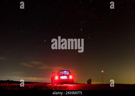 Ein Auto auf dem Hintergrund der Sterne mit Nachthimmel, glänzende Galaxie, rote Rücklichter Stockfoto