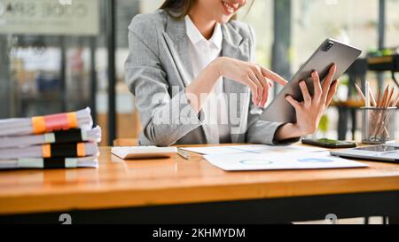 Kurze Aufnahme, wunderschöne junge asiatische Geschäftsfrau oder Chefin, die ein digitales Tablet an ihrem Schreibtisch verwendet. Stockfoto