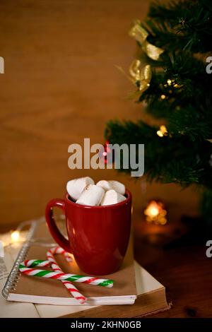 Heiße Schokolade mit Marshmallow in einem roten Becher im Weihnachtsthema im Hintergrund. Stockfoto