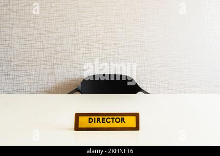 Regieplatte aus Holz auf weißem glänzenden Tisch mit leerem Stuhl im Zimmer Stockfoto