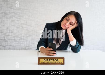 Junge, weiße, brünette Geschäftsfrau, Direktorin im Büro, sitzt am Schreibtisch, benutzt Telefon Scroll Nachrichten, soziale Medien gelangweilt am Arbeitsdirektor lustig. Unnötiges EM Stockfoto