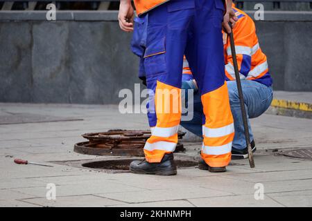 Arbeiter über der offenen Abwasserluke auf einer Straße. Konzept der Reparatur von Abwasser, unterirdischen Versorgungsanlagen, Wasserversorgungssystemen, Kabelverlegung, Wasserrohren Stockfoto