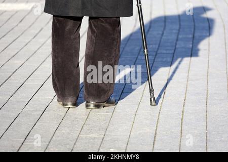 Hinkender Mann mit Gehstock, Schatten auf dem Gehweg. Konzept für Invalidität, Alter Stockfoto