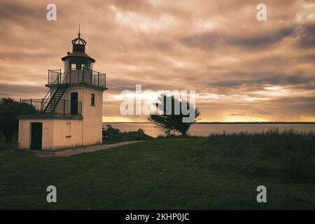 Leuchtturm, Spodsbjerg Fyr in Huntsted an der Küste Dänemarks. Die Sonne scheint durch die Wolken. Wiese mit Bäumen. Landschaftsfoto vom Meer Stockfoto