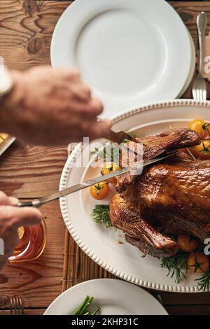 Hände, Essen und den truthahn mit einem älteren Mann zu schnitzen, der ein Messer an einem Esstisch in seinem Haus benutzt. Hühnchen, Thanksgiving und Tradition mit einem Stockfoto