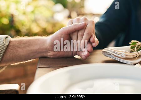 Paare, Händchenhalten und Mittagessen mit Beten, Liebe und Vertrauen in die Ehe, Hoffnung und Fürsorge am Tisch draußen. Mann, Frau und Hand für Hoffnung, Dankbarkeit und Stockfoto