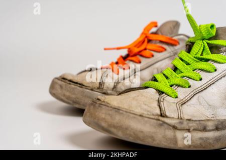 Alte weiße Turnschuhe mit farbigen Schnürsenkeln auf weißem Hintergrund Stockfoto