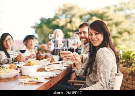 Toast, Wein und Familie zum Mittagessen in einem Garten während einer Weihnachtsfeier auf der Terrasse. Essen, Alkohol und Porträt von Freunden mit einem Jubel und Essen in einem Stockfoto