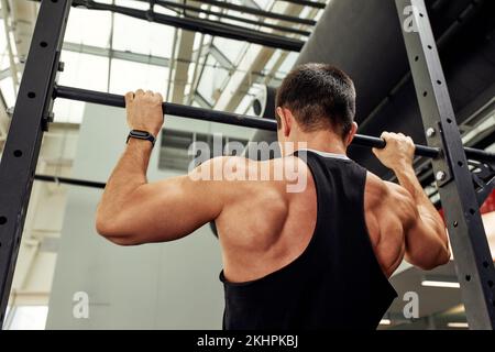 Arbeiten Sie mit eigenem Gewicht, der Athlet macht Übungen auf den unebenen Balken Stockfoto