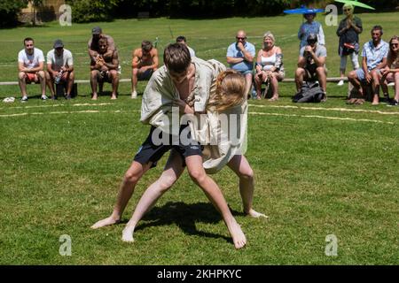 Ein junges Teenager-Mädchen, das mit einem Jungen kämpft, der beim Grand Cornish Wrestling Tournament auf dem malerischen Dorfgrün von St. Mawgan in Pydar i teilhat Stockfoto