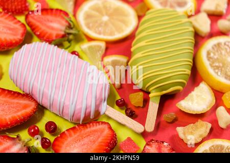 Zwei Eis auf einem Stock - Erdbeere und Zitrone auf gelb-rotem Hintergrund. Sommerobstdesserts. Stockfoto