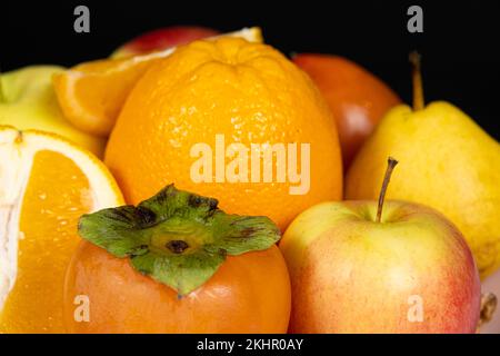 Früchte von orangen und gelben Farben - Äpfel, Kaki, Birnen und Orangen auf schwarzem Hintergrund Stockfoto