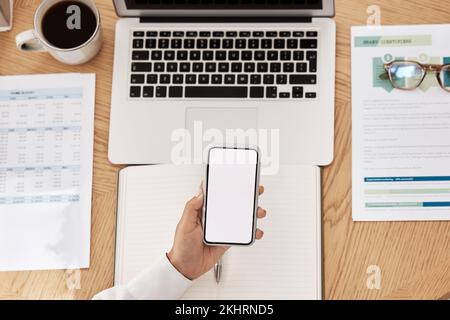 Laptop, Papierkram und Telefon mit Mockup-Platz an einem Schreibtisch in einem modernen Büro, das an einem Projekt arbeitet. Eine Tasse Kaffee, ein Computer und eine Hand mit einem Smartphone Stockfoto