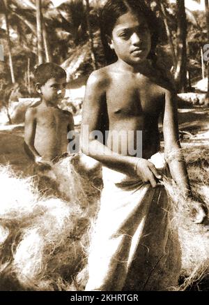 Foto aus den 1940er Jahren von Kindern an der Küste Malabars, die Kokos herstellen, auch Kokosfaser genannt, eine natürliche Faser, die aus der äußeren Hülle der Kokosnüsse gewonnen wird. Es gibt weiße und dunkle oder braune Sorten, die aus unreifen und reifen Kokosnüssen hergestellt werden. --- ۱۹۴۰ کی دہائی میں مالابار ساحل کے بچوں کی تصویر جس میں ناریل کے بیرونی بھوسے سے نکالا جانے والا ایک قدرتی ریشہ کائر/ ناریل کا ریشہ تیار کیا گیا تھا۔ -- 1940 के दशक की मालाबार तट के बच्चों की तस्वीर में नारियल की बाहरी भूसी से निकाले गए एक प्राकृतिक फाइबर कॉयर/नारियल फाइबर का उत्पादन किया गया था। Stockfoto