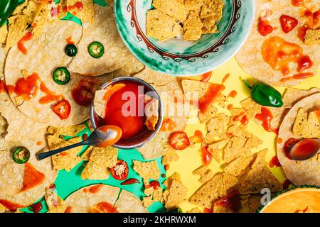 Bunte Tex-Mex-Speisen mit Tropfen und Flecken aus Soße. Blick von oben auf mexikanisches Essen mit Tortilla-Chips. Heiße Jalapenos-Sauce. Chili-Pfeffer. Stockfoto