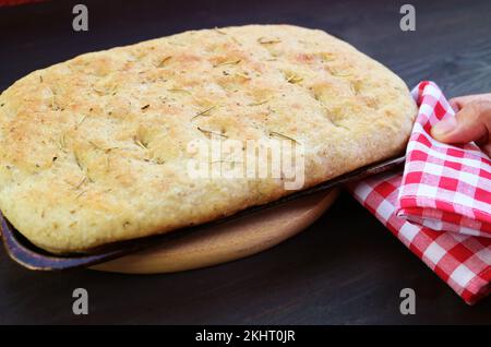 Legen Sie eine Pfanne mit frisch gebackenem Kräuterbrot Focaccia von Hand auf das Breadboard Stockfoto