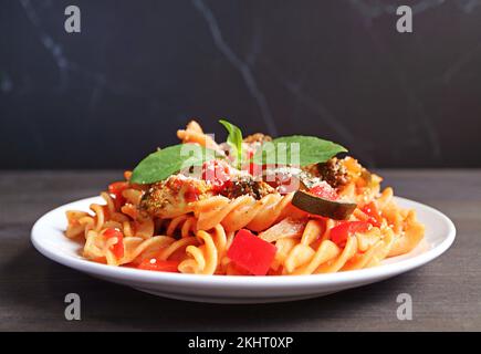Ein Teller mit köstlicher Fusilli-Pasta in Tomatensauce im schwarzen Hintergrund Stockfoto