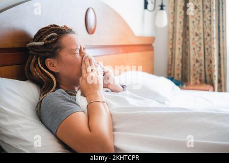 Die Frau liegt im Bett mit einem Taschentuch, das ihr an die Nase gedrückt wird Stockfoto