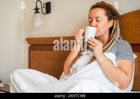 Frau mittleren Alters, die morgens Kaffee im Bett trinkt Stockfoto