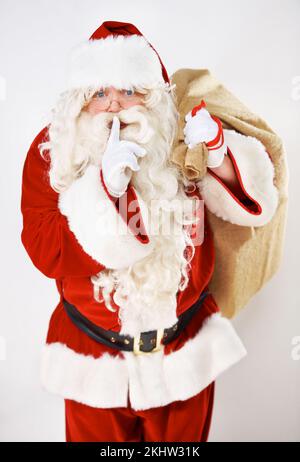 Weihnachtsmann, weihnachtsmann und heimliches Flüstern eines fetten Weihnachtsmanns mit Geschenk und Geschenktüte. Feier eines stillen weihnachtsmanns mit Brillenlächeln Stockfoto