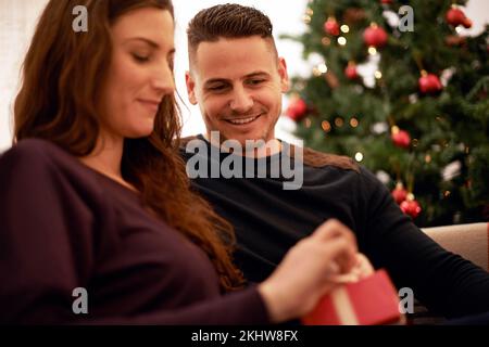 Ein Geschenk, weihnachten und ein Paar entspannen sich zusammen für ein festliches Feiertagsfest. Happy, smile and Surprise Gift Box zur Feier von Weihnachten, Liebe und Glück Stockfoto