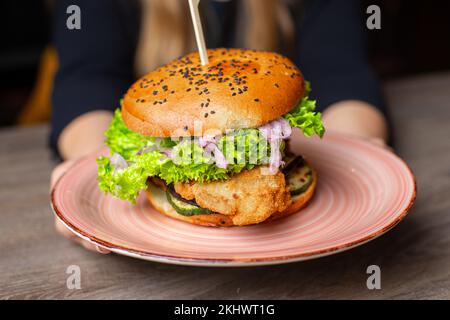 Großer, leckerer Hamburger mit Spieß auf dem Teller im Restaurant. Rindfleisch, Schweineburger mit knusprigen Brötchen, schwarzer Sesam Stockfoto