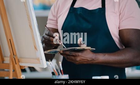 Nahaufnahme der männlichen Hände nicht erkennbarer afrikanischer Maler, der eine Palette mit hellen Öl-Acryl-Farben hält, Farben, auf denen Bilder erstellt werden Stockfoto