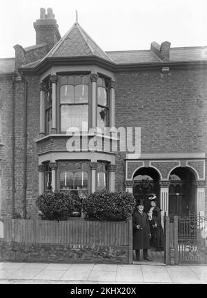 Ein spätes viktorianisches englisches Schwarzweißfoto, auf dem ein älterer Mann und eine ältere Frau in edler Kleidung vor ihrem Haus stehen. Stockfoto