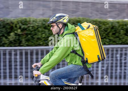Schneller Liefermann fährt in der Stadt, junger Kurier in Technik- und Sportkleidung, mit Helm und Rucksack für Essen, Schwenkeffekt, schnell Stockfoto