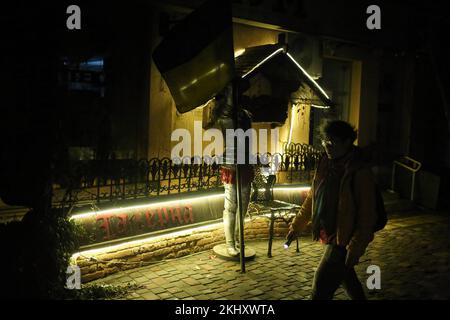 Eine Frau mit einer Taschenlampe, die an der Figur eines Ritter vorbeiläuft, der die Flagge der Ukraine in der Bunin Street hält. Russische Raketenangriffe auf Kraftwerke führten in einigen Regionen zu einem vollständigen Stromausfall. Insbesondere stand Odessa vor großen Schwierigkeiten, und alle Kernkraftwerke, die meisten Wärme- und Wasserkraftwerke blieben ebenfalls stromlos. Die meisten Geschäfte und Cafés werden von Generatoren angetrieben. Der elektrische Nahverkehr funktioniert nicht; die meisten Wohngebäude und kritischen Infrastrukturanlagen sind stromlos. Stockfoto