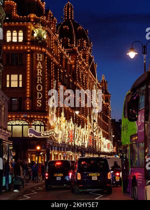 Harrods berühmtes Kaufhaus in Knightsbridge mit Weihnachtsausstellung. Fußgänger und Verkehr vor dem Hotel, einschließlich Taxis. Nach London. Stockfoto