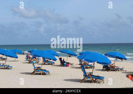 Delray Beach mit blauen Liegestühlen und Sonnenschirmen, blauem Himmel und Wolken im Hintergrund. Stockfoto