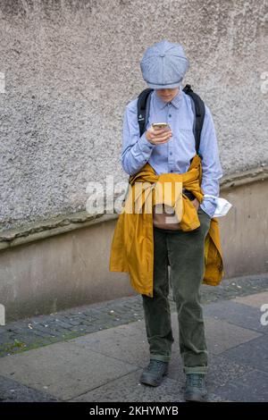 Ein frecher Tourist, der auf jedes Wetter vorbereitet ist, überprüft die Wegbeschreibung auf seinem Telefon, bevor er die Royal Mile von der Cockburn Street in Edinburgh erreicht. Stockfoto