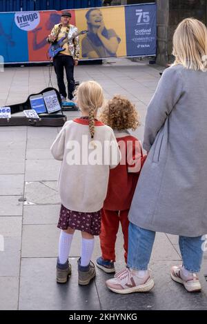 Kleine Menschenmenge. Zwei kleine Kinder und ihre Mutter sehen einem Straßenkünstler von Edinburgh Fringe zu, der seine Show auf der historischen Royal Mile von Edinburgh beginnt. Stockfoto