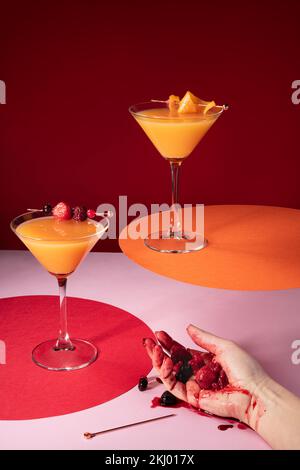 Szene mit der Hand einer betrunkenen Frau, die zerbrochene Beeren mit Orangensaft-Cocktails hielt. Moderne, lebendige Farben. Stockfoto