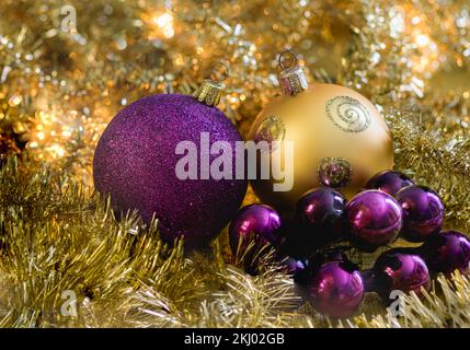 Lila und goldene weihnachtskugeln mit goldenen Girlanden und leuchtenden weihnachtslichtern im Hintergrund. Stockfoto