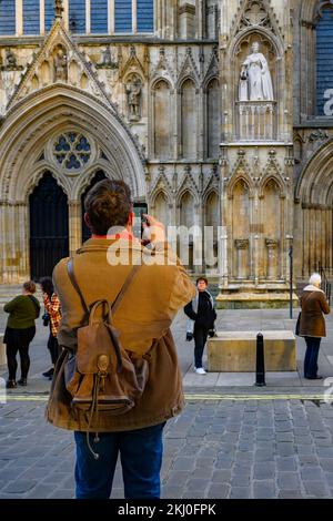 Person, die eine Handykamera verwendet (Aufnahme der neuen Elizabeth 2-Statue auf Nische und stehende Besucher) - York Minster Westfront, North Yorkshire, England, Großbritannien. Stockfoto