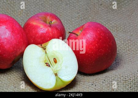 Mehrere rote Äpfel mit einem in zwei Hälften geschnittenen Apfel, die das Innere und die Kerne freilegen. Stockfoto