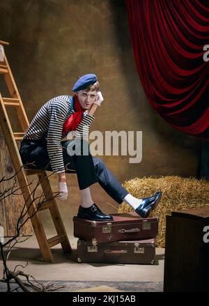 Porträt eines männlichen Pantomime-Künstlers, der Traurigkeit und Einsamkeit vor dunklem Retro-Zirkus-Hintergrund ausdrückt. Das Konzept menschlicher Emotionen, Kunst, Mode Stockfoto
