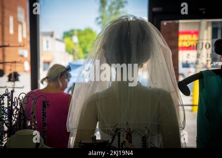 Eine Frau verlässt den Laden mit einer Schaufensterpuppe in Brautkleidung im Vordergrund Stockfoto