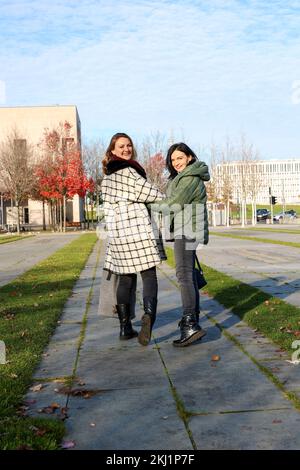 Zwei Frauen, die in Mänteln auf einer Straße in der Stadt spazieren Stockfoto