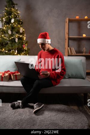 Junger Mann mit Laptop-Computer und Kreditkarte zu Hause in Santa hat. Technologie, Shopping, Banking, Home und Lifestyle Stockfoto