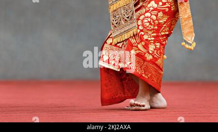 Asiatischer Reisehintergrund. Wunderschöne balinesische Tänzerin in traditionellem Sarong-Kostüm, Tanz, Legong-Tanz. Beinbewegungen. Kunst, Kultur Indonesiens Stockfoto