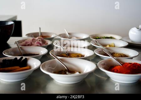 Viele verschiedene Gewürze in Keramiktellern mit Löffeln, in der Küche, zubereitet für traditionelle indische Fisch-Curry Stockfoto