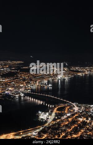 Eine vertikale Antenne der Tromso-Brücke mit der nächtlichen Skyline der Stadt Tromso, Norwegen Stockfoto