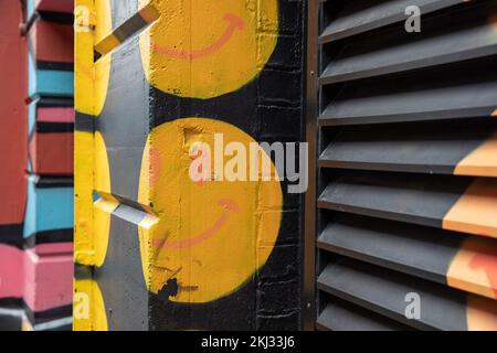 Nahaufnahme von farbenfrohen Kunstwerken an der Wand und den Fensterläden, eines Gebäudes in einer Stadtstraße in Shoreditch, East London, E1. Stockfoto