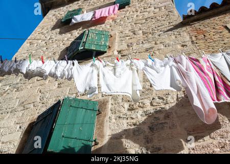 Wäscheleine mit pinkfarbener und weißer Wäsche, die an Steinwänden mit grünen Fensterläden trocknet, Kotor, Montenegro Stockfoto