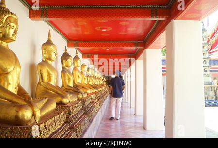 Besucher bestaunen die „Row of Sitting Postured Buddha Images“ im Kloster namens Phra Rabiang des Tempels des liegenden Buddha in Bangkok, Thailand Stockfoto